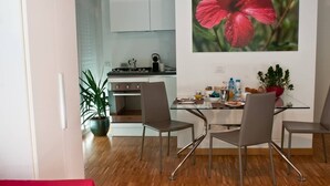 A modern kitchen with white cabinets, a dining area with a glass table and metal chairs, and a potted plant. - Vela Suites H Milan center with garage (Milano)