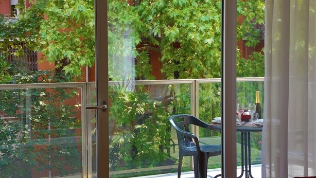 A balcony with a glass door, a table with a bottle and glasses, and a chair. - Vela Suites H Milan center with garage (Milano)