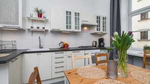 A modern kitchen with white cabinets, a black countertop, and a wooden dining table with placemats. - AT Krakow Apartments (Kraków)