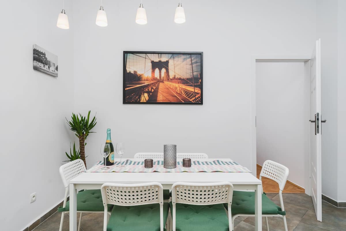 Uma área de refeições com uma mesa posta para dois, uma moldura acima e uma porta à direita.