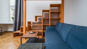 A modern living room with a blue sofa, wooden shelving, and a small table with decorative items. - AT Krakow Apartments (Kraków)