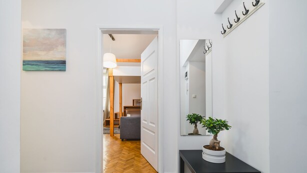 A hallway with a wooden floor, a black table with a potted plant, and a painting on the wall. - AT Krakow Apartments (Kraków)