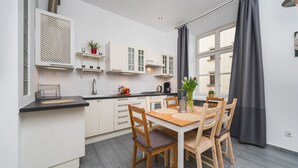 A modern kitchen with white cabinets, a black countertop, and a wooden dining table with four chairs. - AT Krakow Apartments (Kraków)