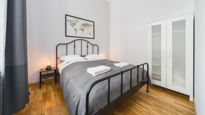 A neatly made bed with a grey bedspread and white pillows, a small bedside table with a lamp, a world map on the wall, and a sliding glass door closet. - AT Krakow Apartments (Kraków)