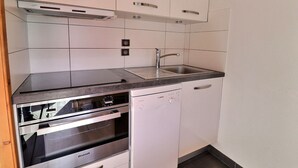 A compact kitchen with a Bosch dishwasher, a Brandt oven, a stainless steel sink, and white cabinetry. - Lovely Quiet Duplex, South Facing, On the Slopes, 2* for 5 People (Méribel)
