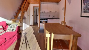 A wooden dining table with chairs, a staircase, and a kitchen in the background. - Lovely Quiet Duplex, South Facing, On the Slopes, 2* for 5 People (Méribel)