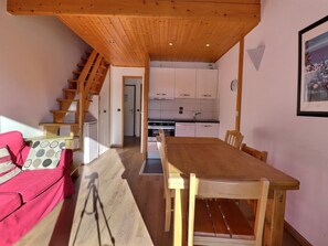 Una mesa de comedor de madera con sillas, una escalera y una cocina al fondo.