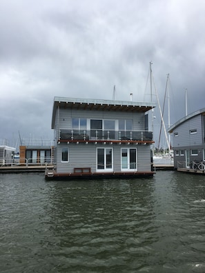 Une maison flottante dotée d’un balcon, de grandes fenêtres et offrant une vue sur l’eau.