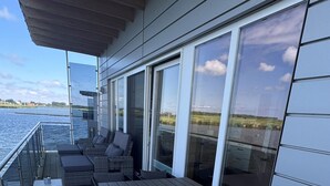 En utomhusveranda med grill, sittplats och stora fönster med utsikt över en sjö eller annat vattendrag.