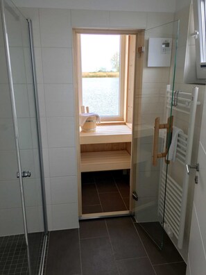 Une salle de bain avec une douche, une fenêtre donnant sur un plan d’eau, un porte-serviettes et un radiateur.