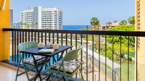 Un balcon avec une table et des chaises, offrant une vue sur le paysage urbain et l’océan.