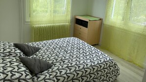Ein Schlafzimmer mit einem Bett, einem Schminktisch und einem Fenster mit gelben Vorhängen.