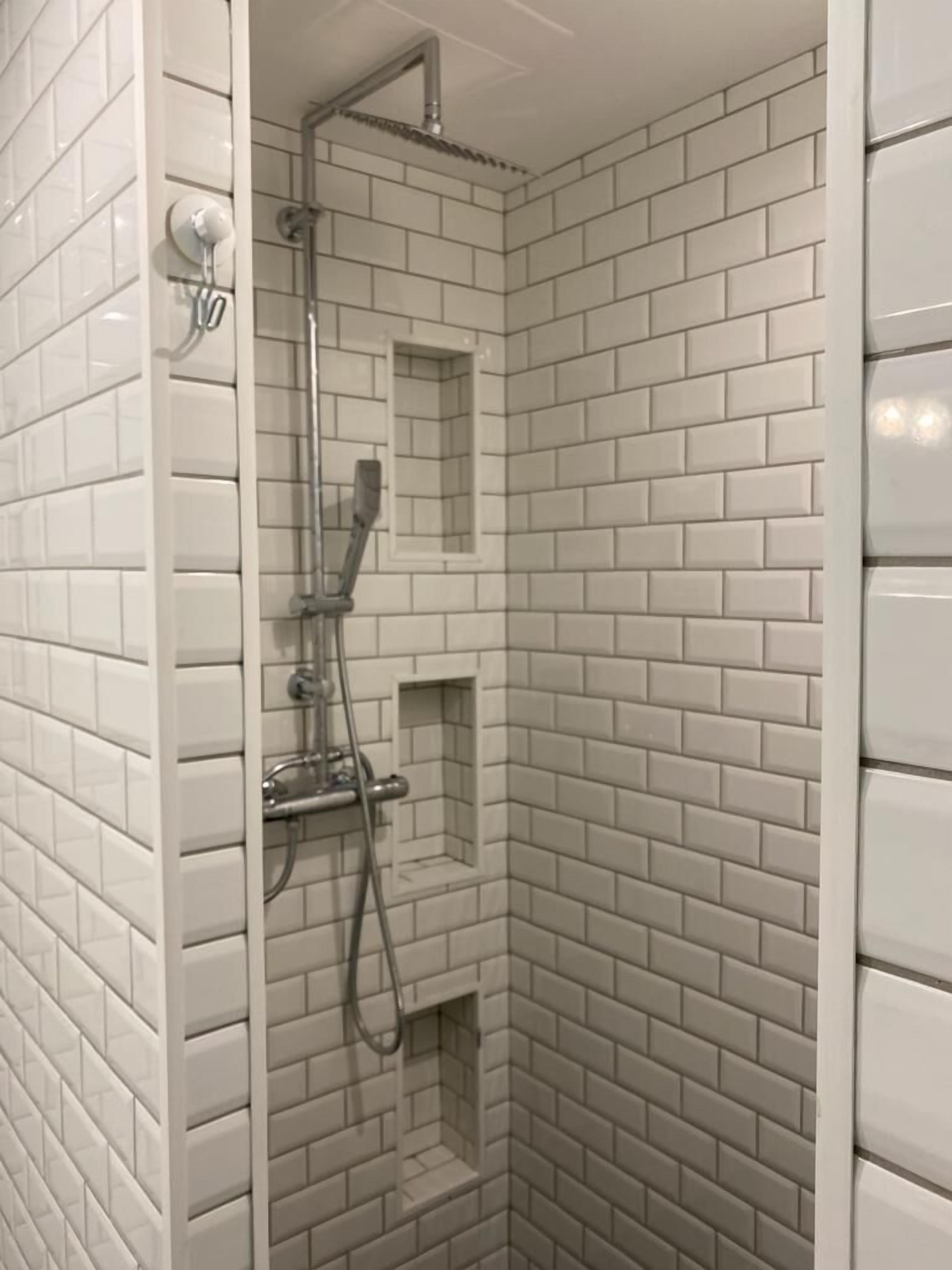 A shower with white subway tile walls and a corner showerhead.