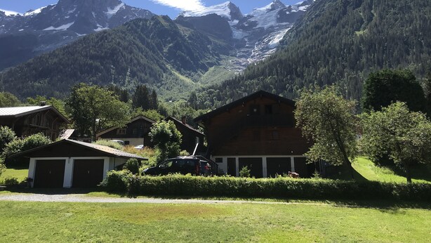 Eine Berglodge mit Holzbalkon, einer Garage und Blick auf verschneite Berggipfel.