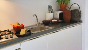 Une cuisine moderne équipée d’une cuisinière à gaz, d’un évier et de divers ustensiles, notamment une planche à découper, des bols et une plante en pot.