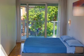 A bedroom with a large bed, a view of a balcony with greenery, and a sliding glass door. - Vela Suites N Milan center with garage (Milano)
