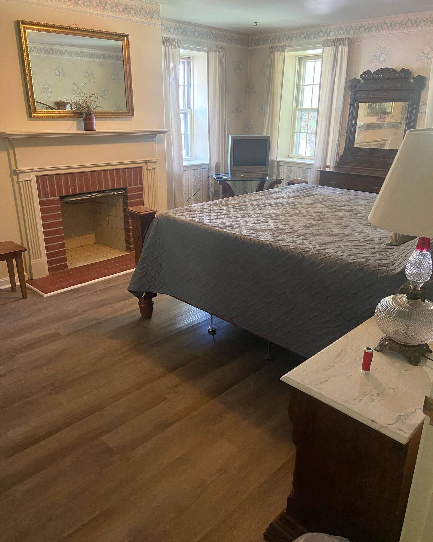 A bedroom with a large bed, a fireplace, a television, and a lamp on a side table.