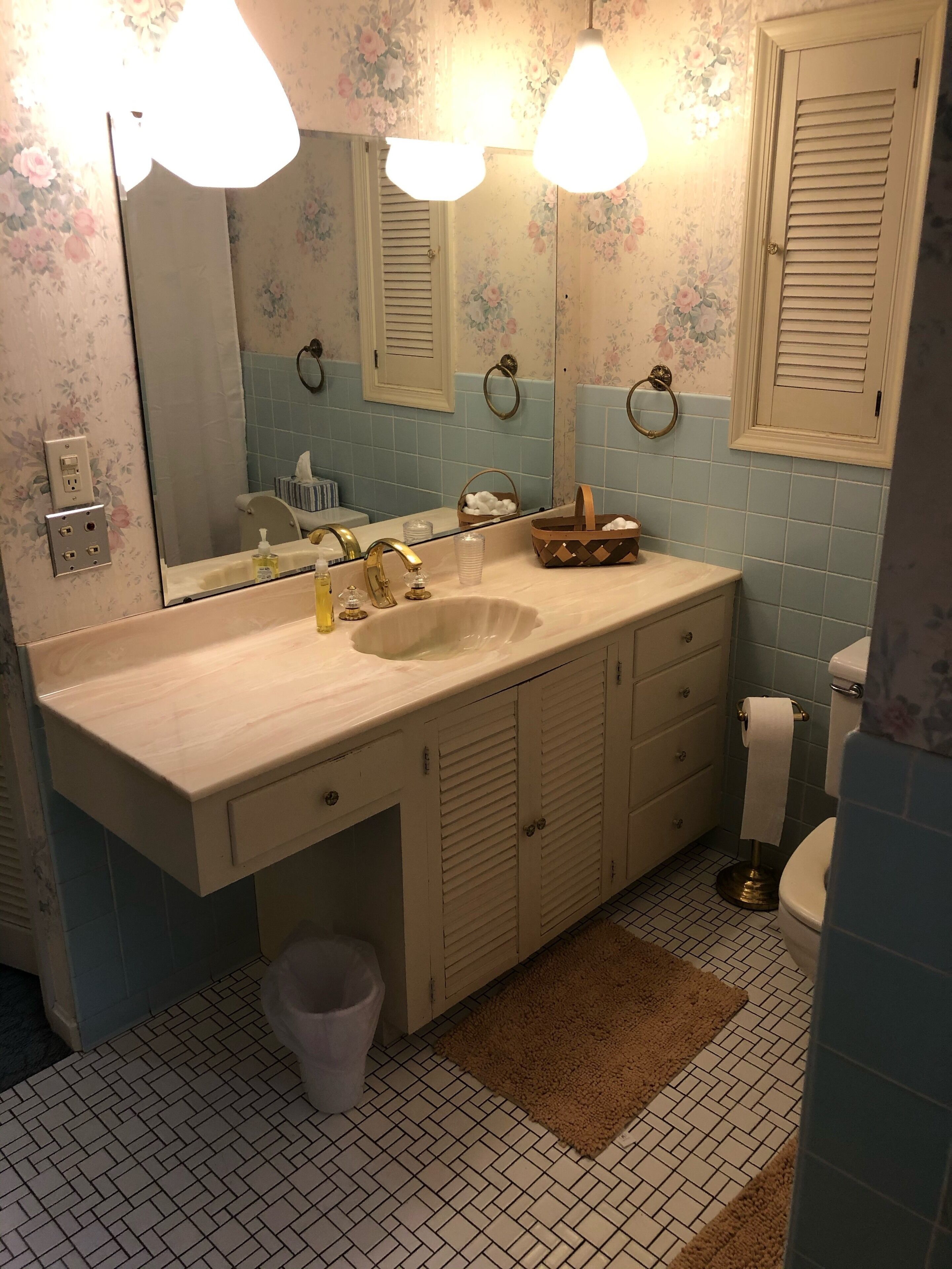 Ein Badezimmer mit einem großen Spiegel, zwei Wandleuchten, einem Waschbecken inklusive Waschtisch, einer Toilette und einem Mülleimer.