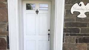 Une porte blanche avec un paillasson sur lequel on peut lire « REMERCIEZ » et une plaque sur le mur indiquant « Maison Weaverling, 1873 ».