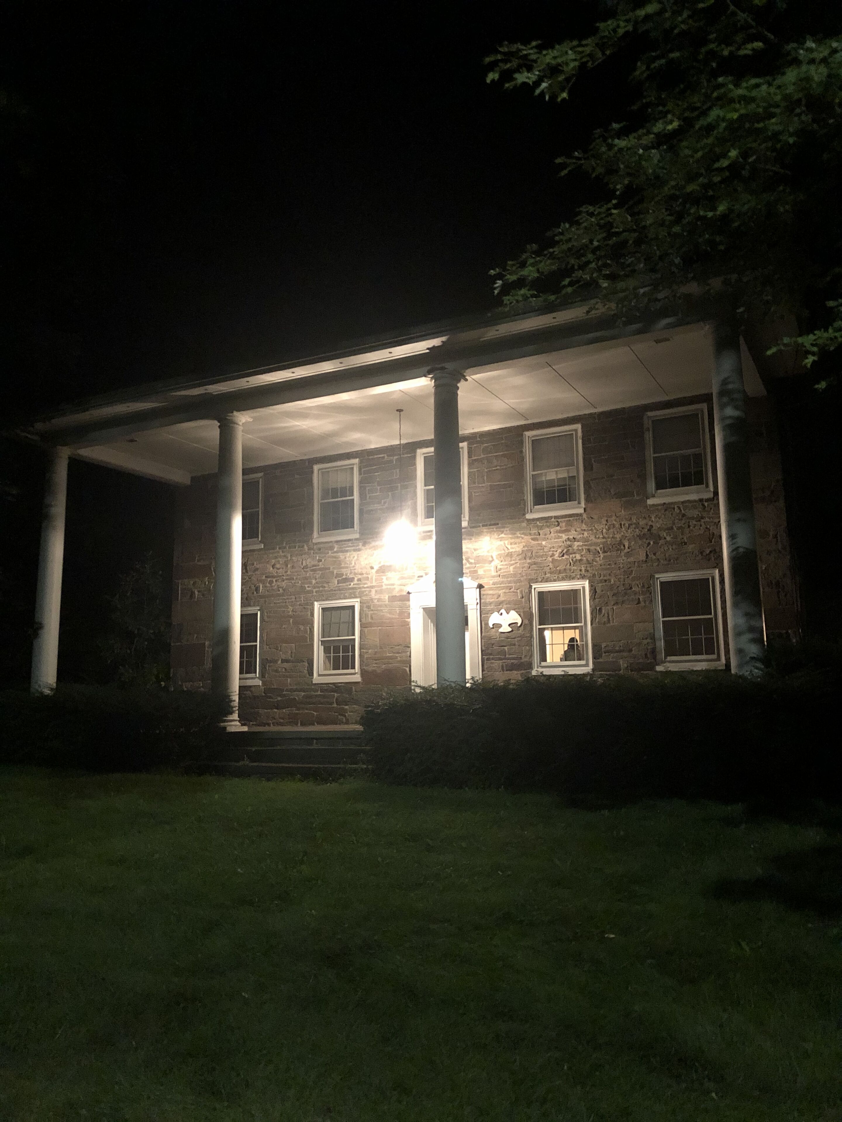 A brick building with a covered porch and columns, illuminated by exterior lighting.