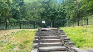 Un escalier en pierre menant au sommet d’une colline, entouré d’une clôture métallique et de verdure.