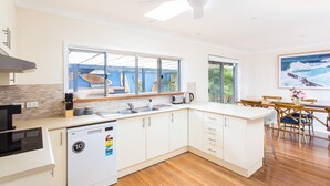 Una cocina moderna con armarios blancos, lavavajillas y un amplio ventanal con vistas a una zona de piscina.