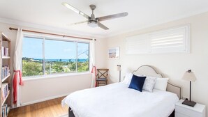 Un dormitorio con cama, ventilador de techo, ventana con vistas, mesita de noche y estantería.