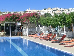A poolside area with lounge chairs and a view of a town in the background. - Santorini Camping & Hostel (Santorini)