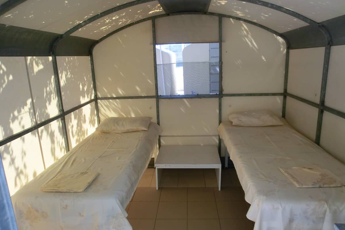 A small, enclosed room with two beds, a bench, and a window.