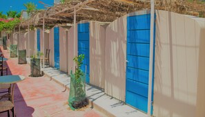 A row of blue doors with beige walls, a tiled floor, and outdoor seating with tables and chairs. - Santorini Camping & Hostel (Santorini)