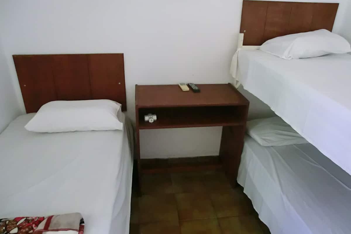 A small, compact room with two single beds, a wooden nightstand with a remote control, and a small table.