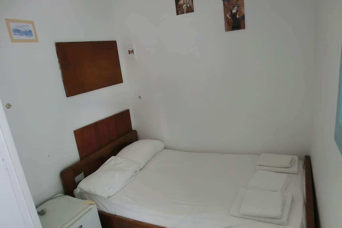 A single bed with a wooden headboard, a small bedside table, and a wall-mounted light switch.