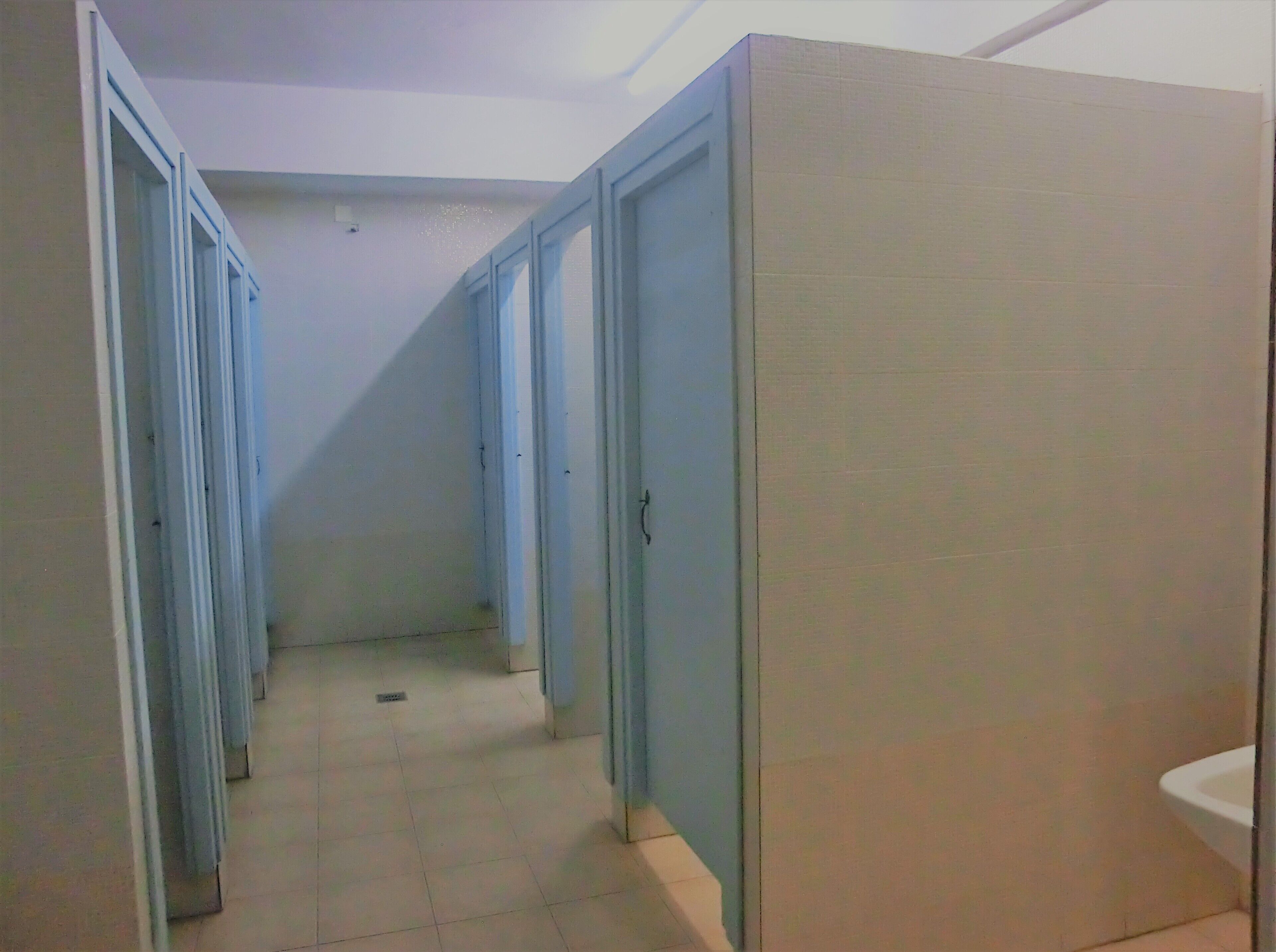 Un couloir étroit avec des portes bleues, un sol carrelé et un lavabo blanc sur le côté droit.