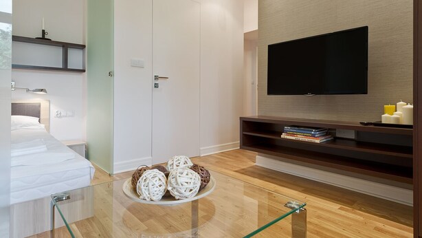 Een moderne hotelkamer met een bed, een glazen salontafel met decoratieve objecten, een flatscreen televisie aan de muur en houten vloeren.
