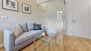 Een moderne woonkamer met een grijze bank, een glazen salontafel en twee ingelijste foto's aan de muur.