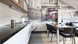 Cozinha moderna com ilha integrada, área de refeições com mesa e cadeiras, e vista para a rua com edifícios e mesas ao ar livre.