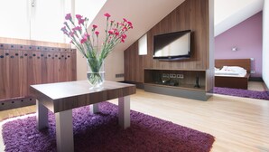 Quarto moderno com televisão na parede, cama com roupa de cama branca e tapete roxo no chão.
