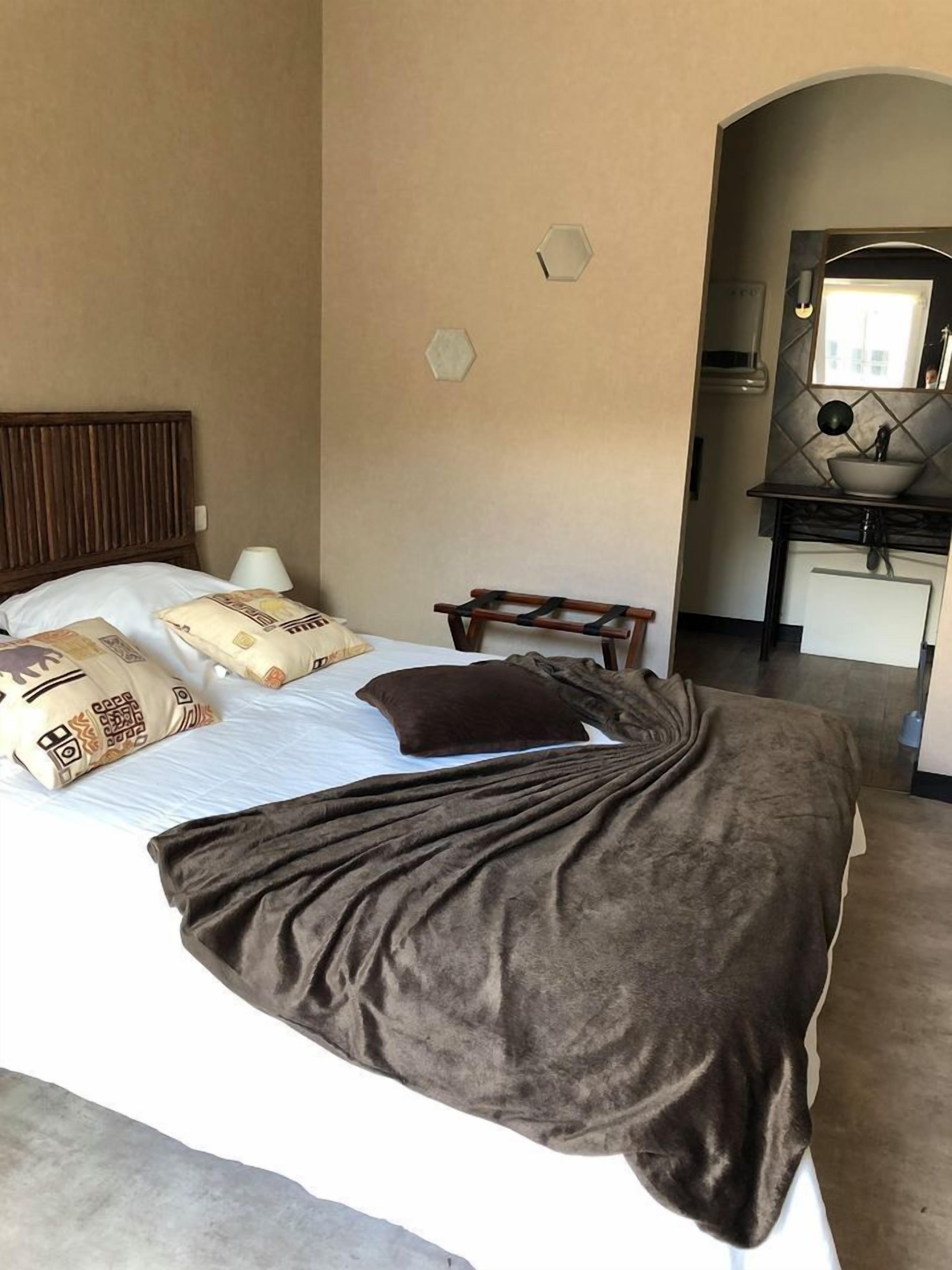 A hotel room with a bed, pillows, a bedside table, a lamp, a mirror, and a small desk with a sink.