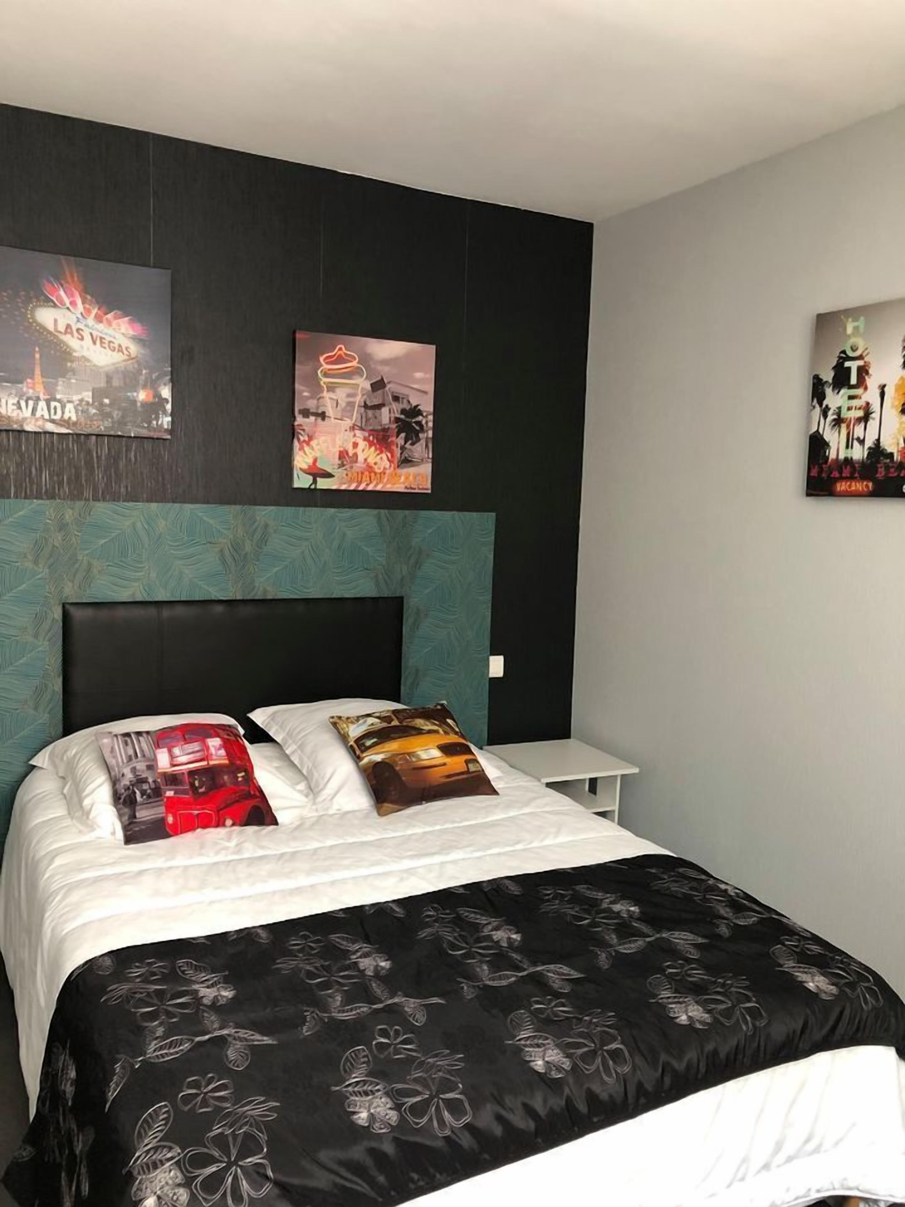 A modern hotel room with a large bed, two pillows, a nightstand, and wall art depicting Las Vegas and a hotel.