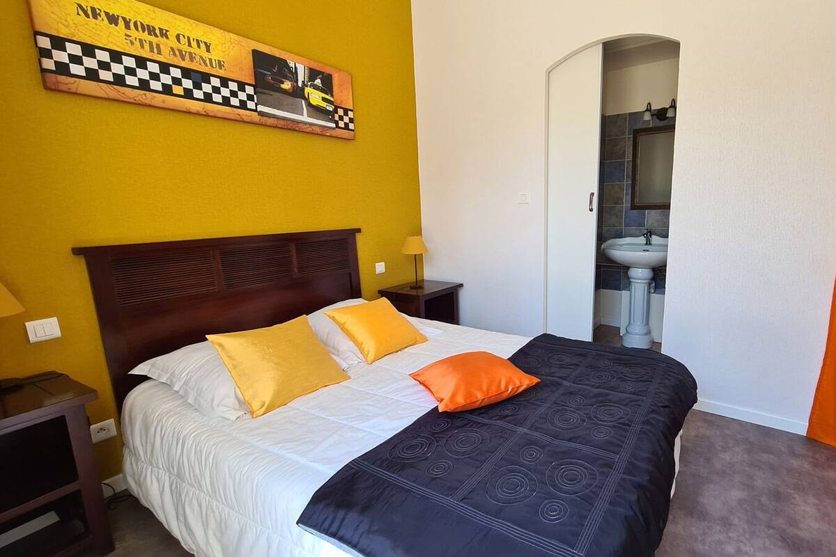 A hotel room with a bed, a nightstand, a lamp, a bathroom with a sink and mirror, and a checkered sign on the wall.