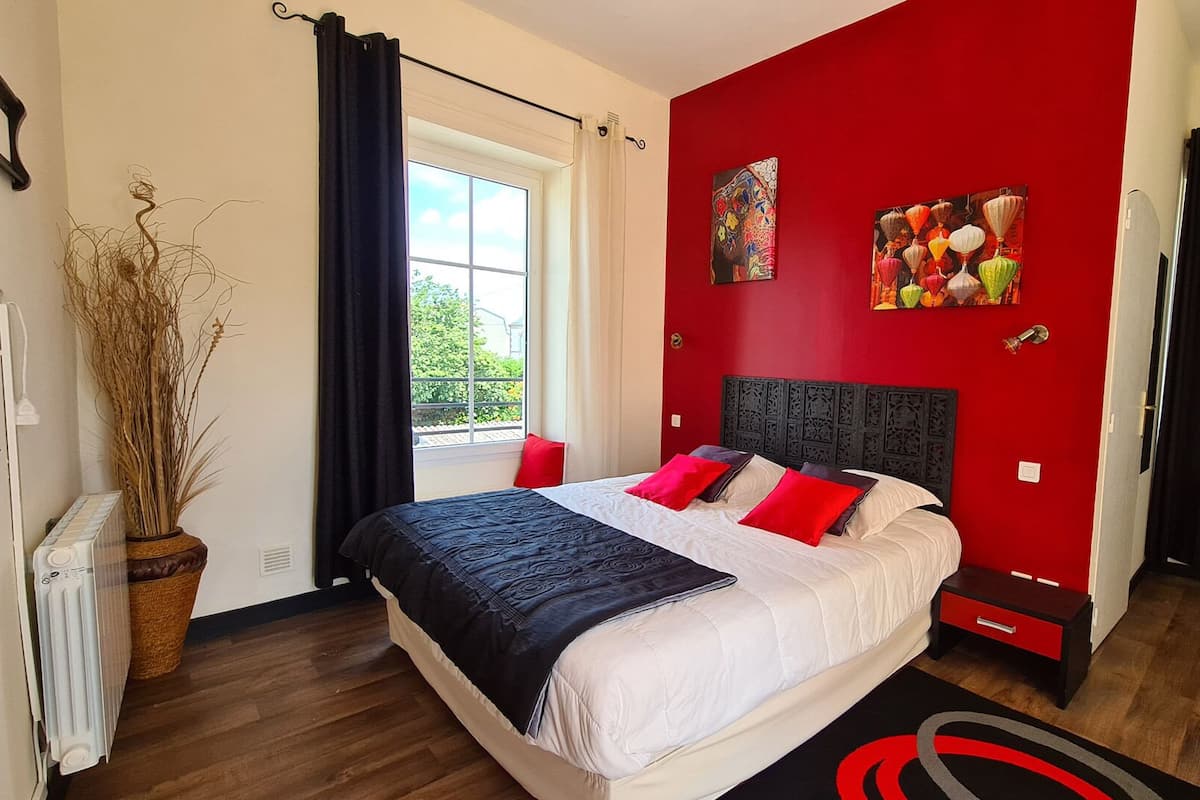 A bedroom with a large bed, red walls, and two paintings.