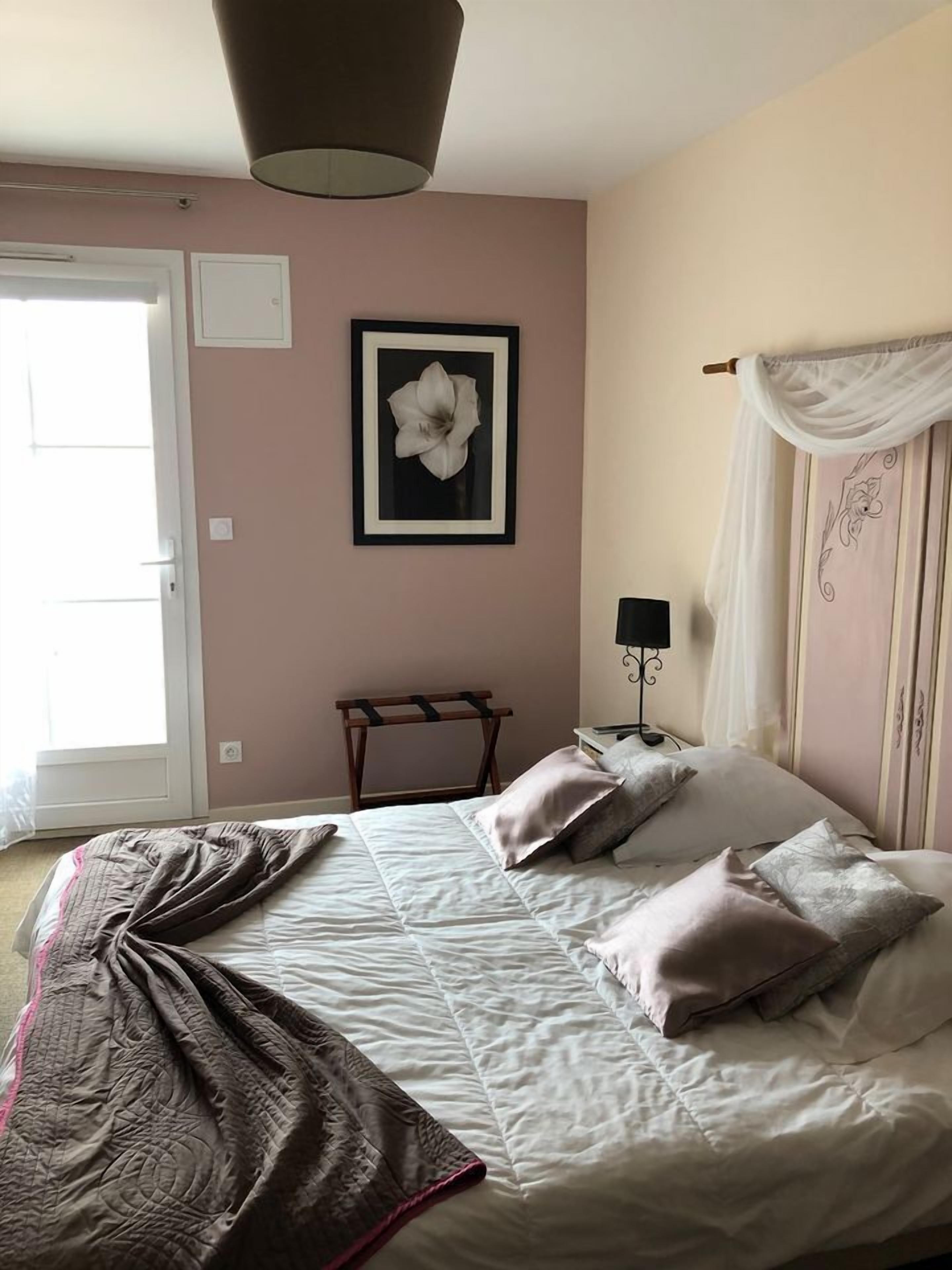 A bedroom with a bed, a bedside table, a lamp, a framed picture on the wall, and a window with curtains.