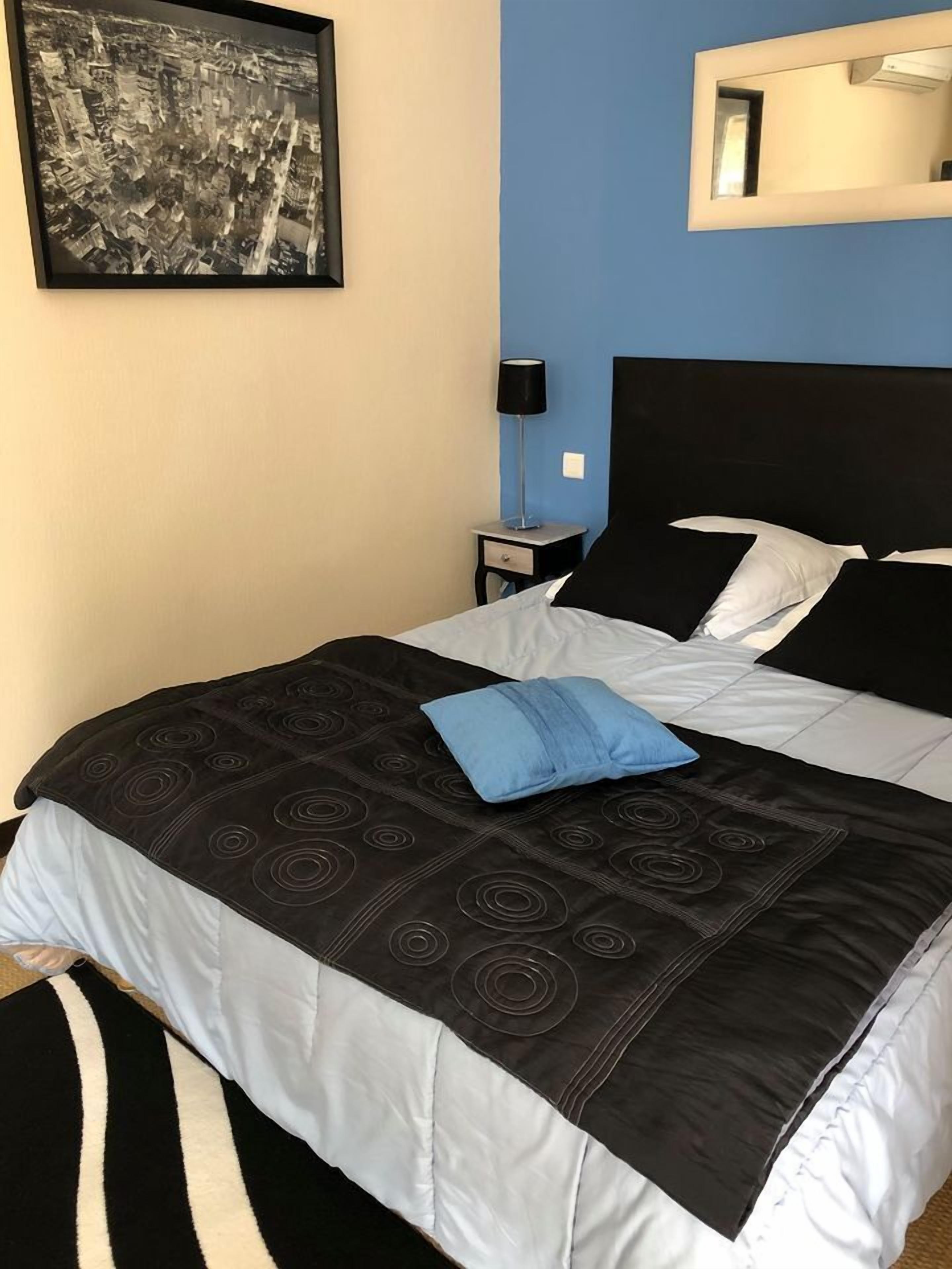 A neatly made bed with a black and white patterned bedspread, a blue pillow, and a black headboard. There is a framed black and white photograph on the wall above the bed.