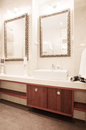 A bathroom with two large mirrors, a white sink, and a wooden vanity with drawers.