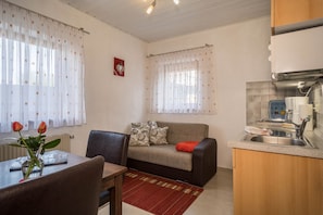 A compact living space with a kitchenette, a sofa, a dining table, and a vase with flowers.