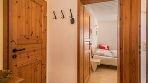 Una puerta de madera con un picaporte, un perchero con ganchos y una cama con almohada roja y cabecera blanca.