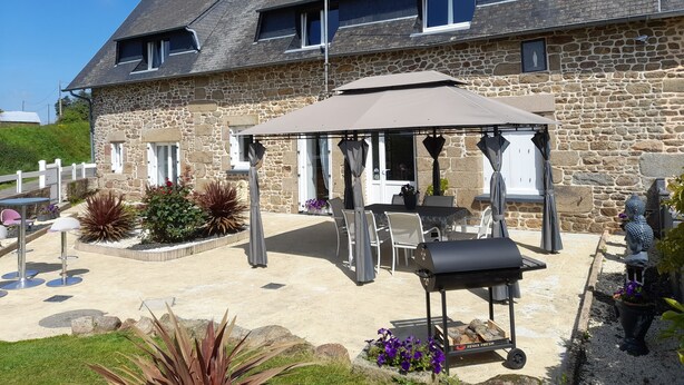 Een stenen huis met een overdekte patio, buiten zitplaatsen en een barbecue.
