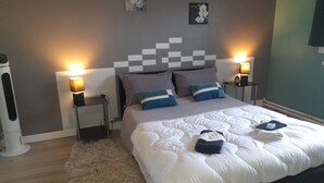 Een netjes opgemaakt bed met een witte deken en blauwe kussens, aan weerszijden geflankeerd door nachtkastjes met lampen, in een kamer met een grijs- en wit kleurenpalet.