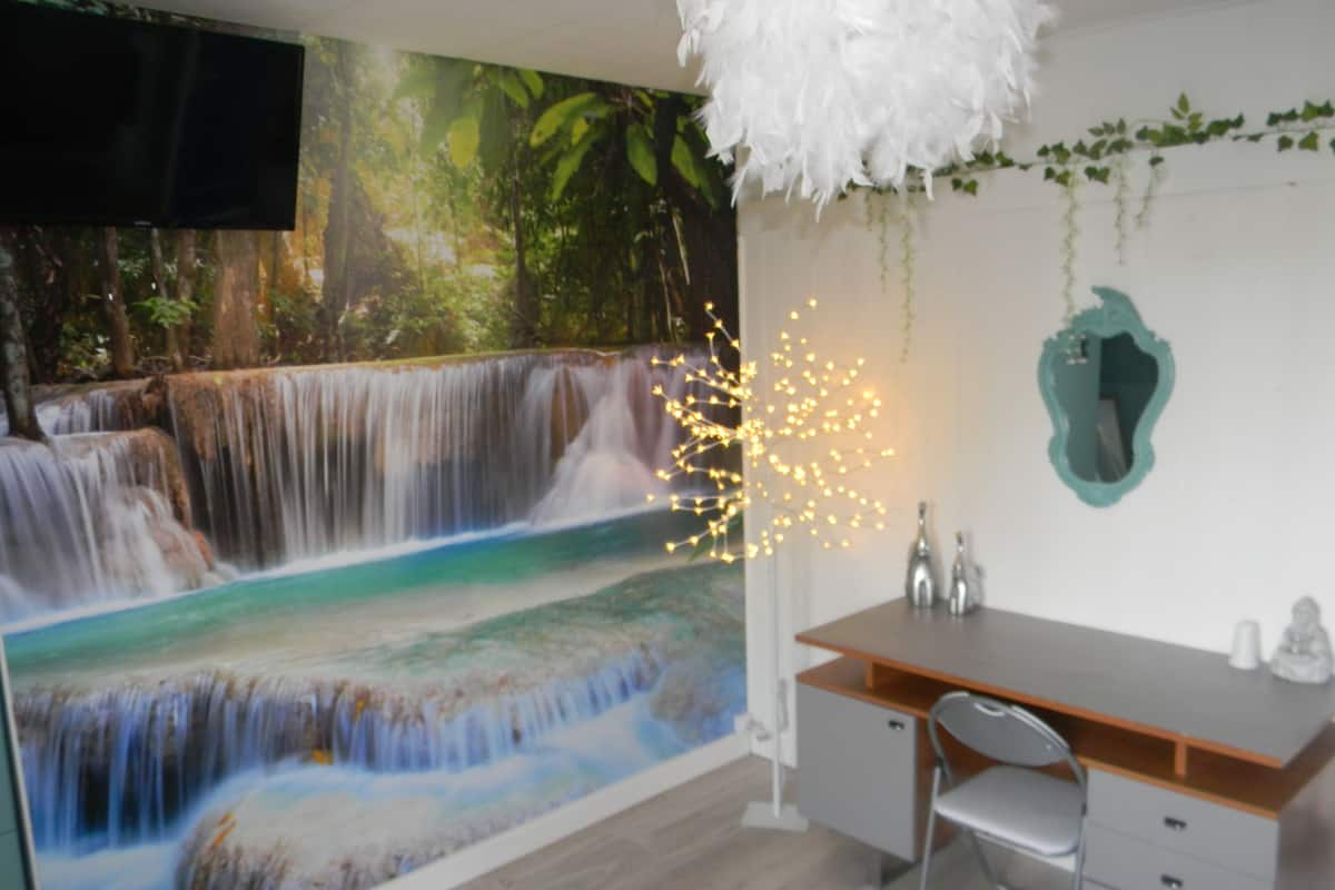 A room with a waterfall mural, a desk with drawers, a chair, and a hanging light fixture.