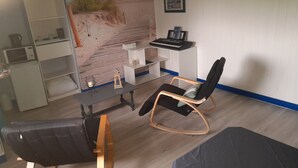 Een kamer met een strandmuur, een bureau met toetsenbord, een schommelstoel, een boekenkast en een magnetron.